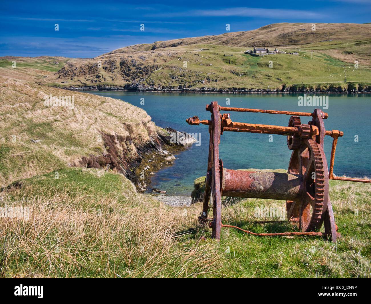 An abandoned, rusting boat winch with beach below in Shetland, UK, taken on a sunny day with blue sea in the background. Stock Photo