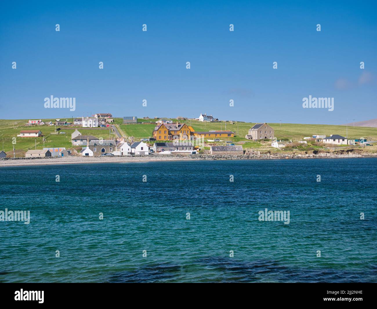 The community of Hillswick in Northmavine, Shetland, UK. Viewed across clear blue water from the Ness of Hillswick on a sunny day Stock Photo