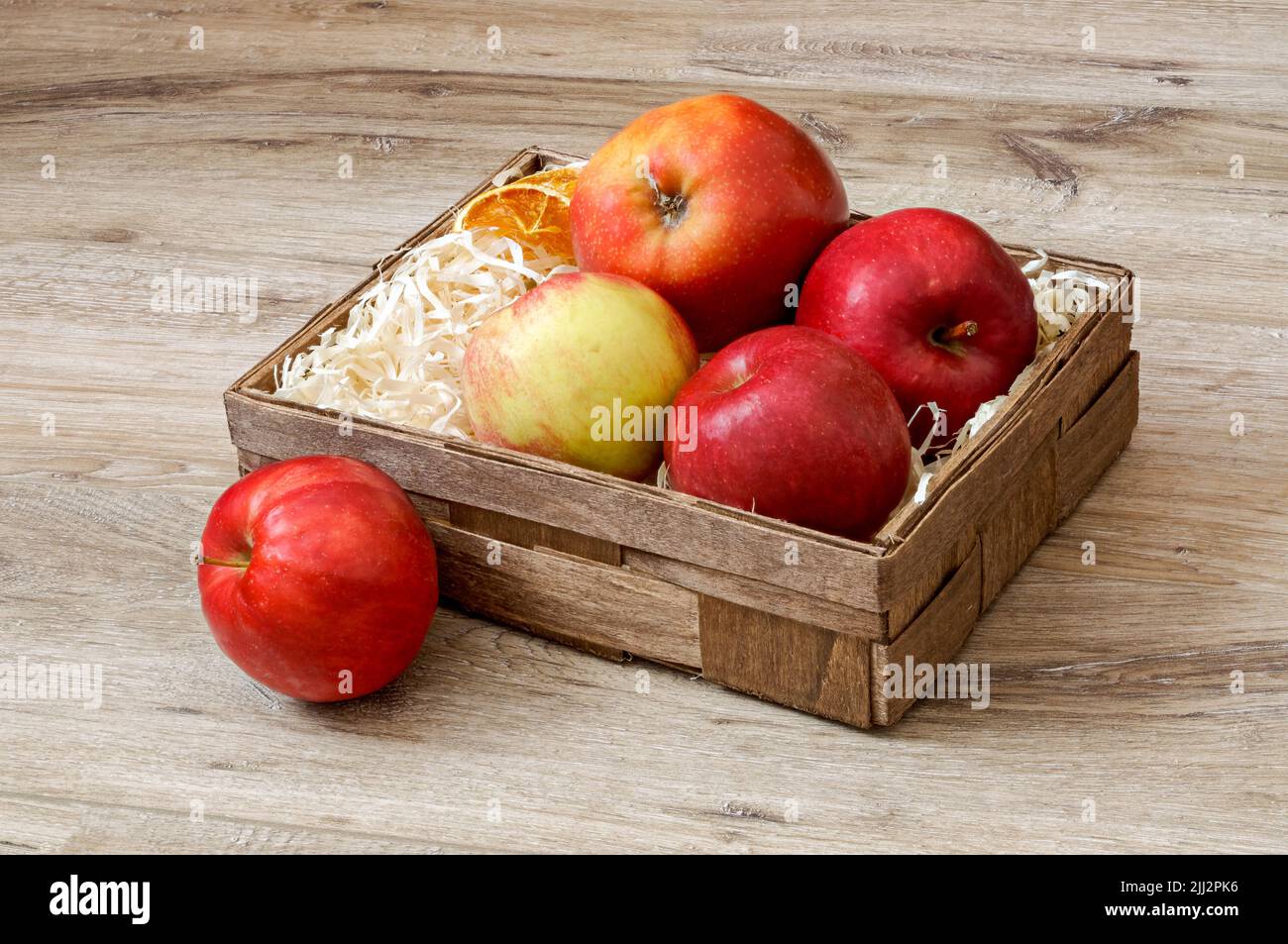 apples in a decorative box lined with wood shavings against the background of a wooden floor from close up, ripe fruit and slices of dried oranges Stock Photo