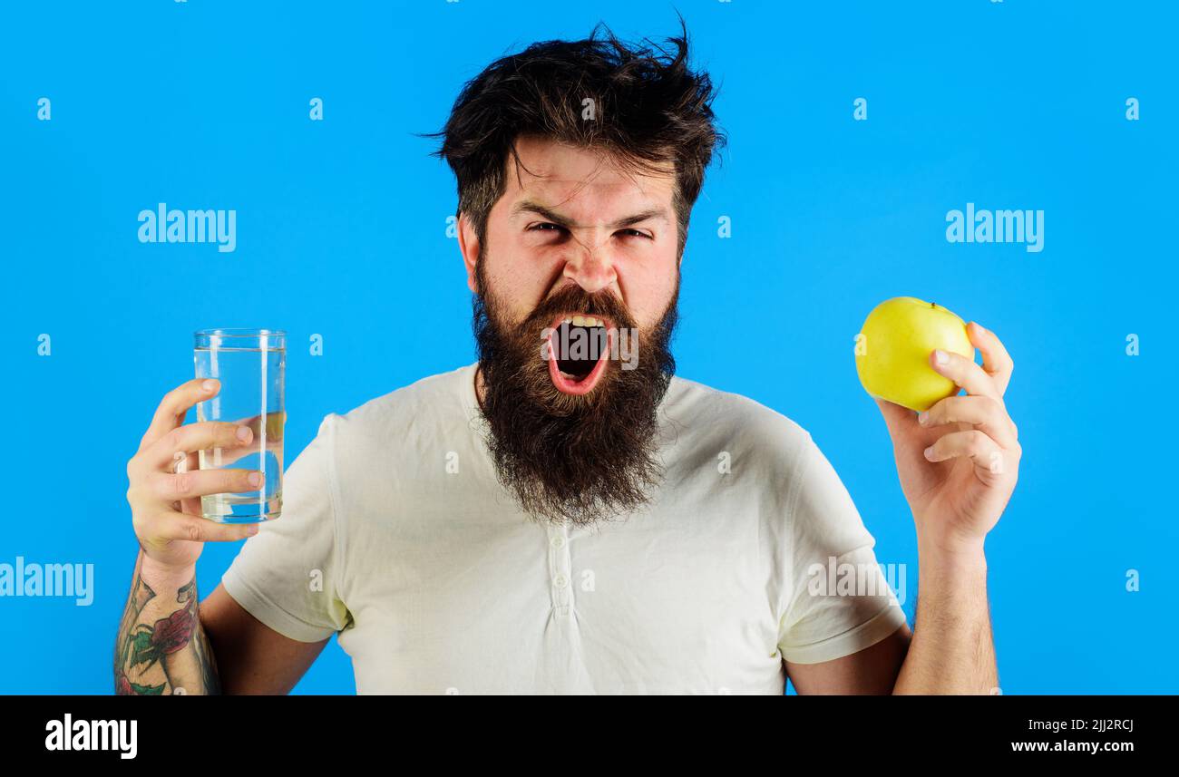 Waking. Sleepy bearded man with glass water and apple. Hydration. Healthy lifestyle and nutrition. Stock Photo