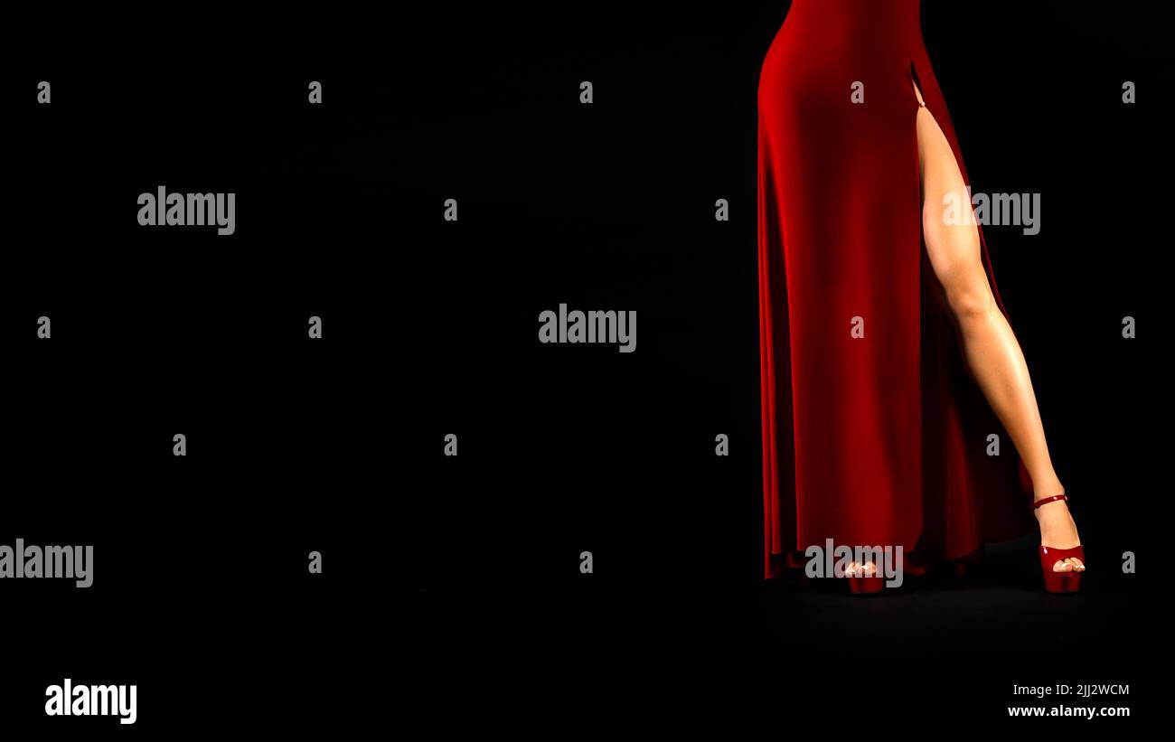 Unrecognizable sexy female legs in a red dress and high heeled shoes on a black background. Stock Photo