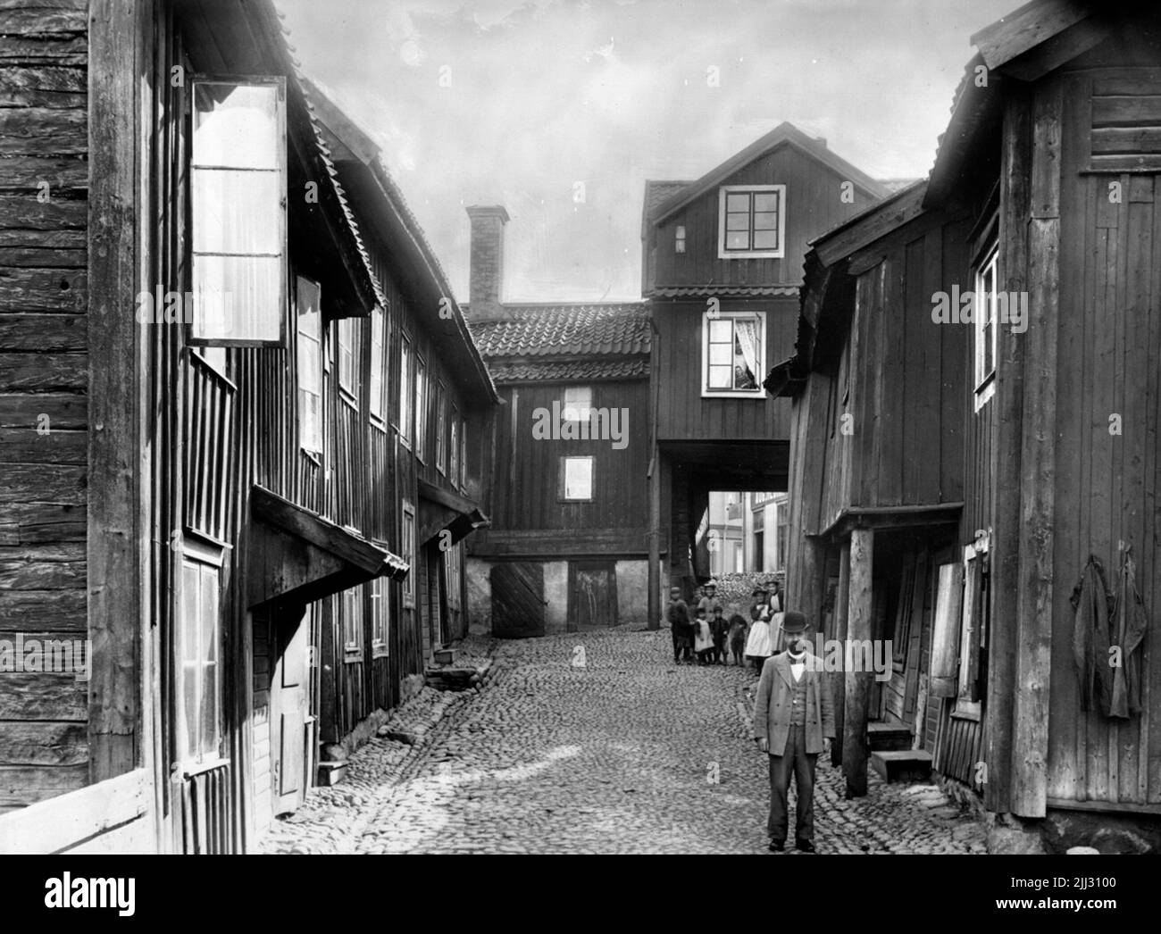 Two -storey residential building in wooden yard interior. Older man and 8 children. Reproduction after a picture from 1905. Stock Photo