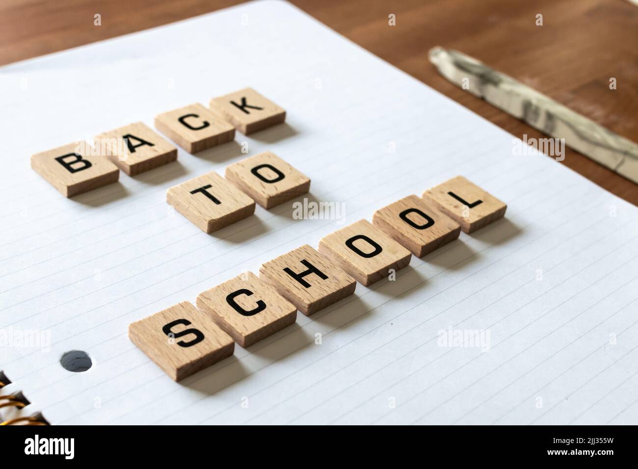 Wooden letters spell out 'back to school' on a blank white lined notepad beside a red apple and a pen. Hardwood desk surface. Learning. Stock Photo