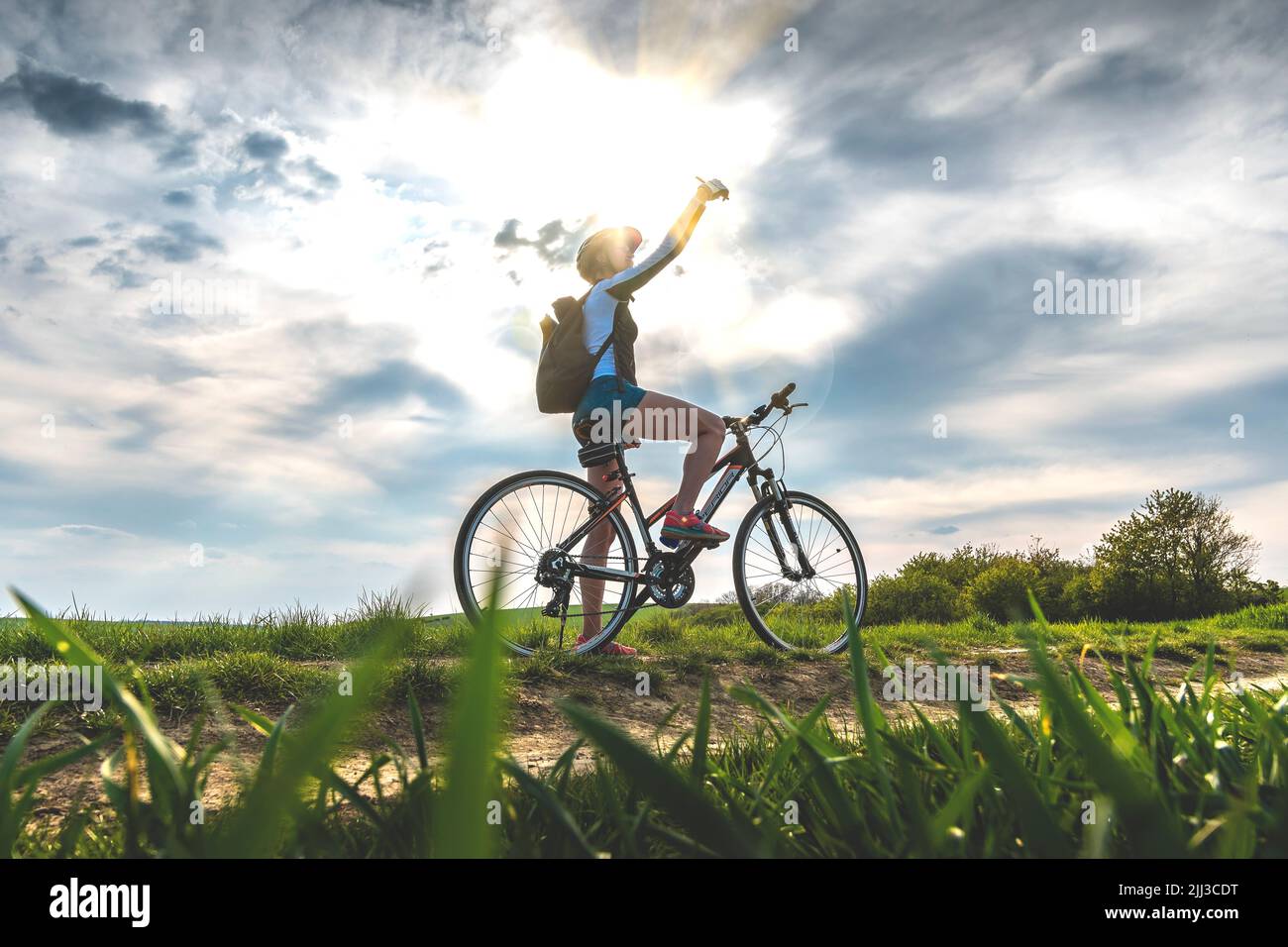 Silhouette of a woman on a bicycle holding a phone. Searching for a telephone signal. Lost cyclist. Smartphone navigation and map applications. Stock Photo