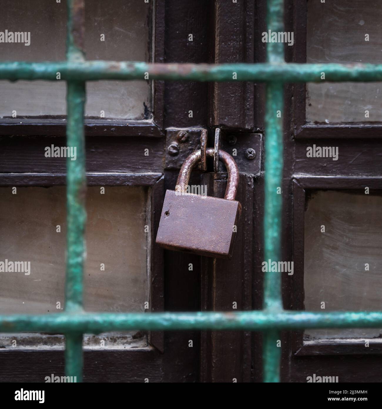 Old padlock on the old wooden door behind a grid Stock Photo