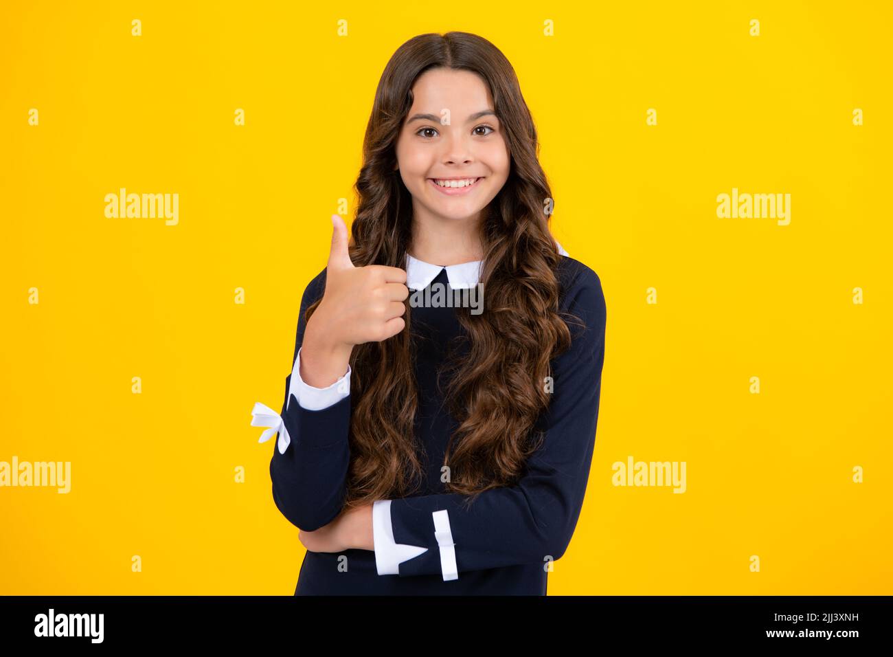 Happy casual teenager child girl showing thumb up and smiling isolated on yellow background. Stock Photo