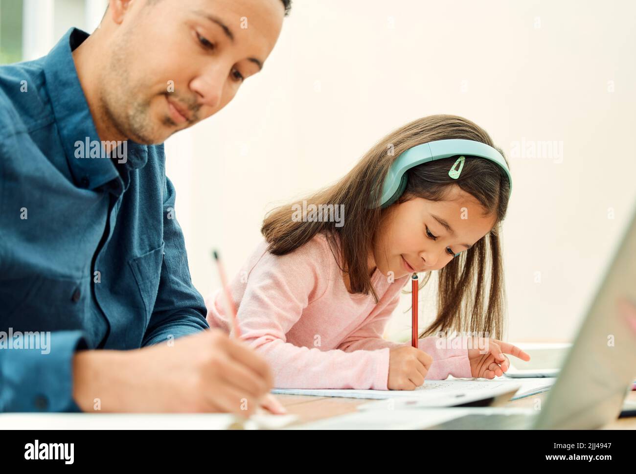 Theyre both working very hard. an adorable little girl doing her homework next to her dad. Stock Photo