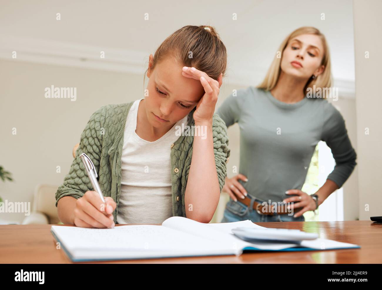 Navigating through a demanding time. a young mother looking frustrated while helping her daughter with homework at home. Stock Photo