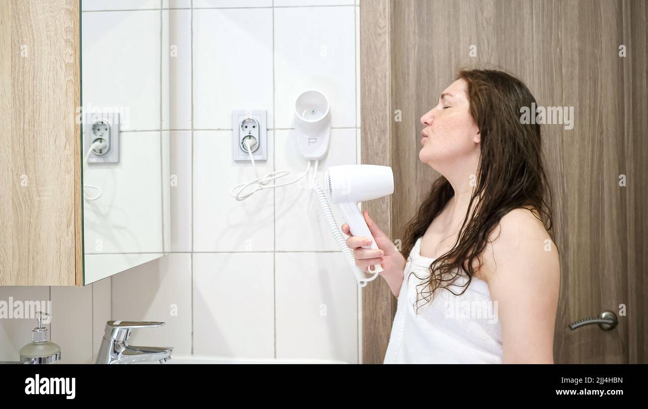 Woman looks in mirror and dries hair with hairdryer dancing Stock Photo ...