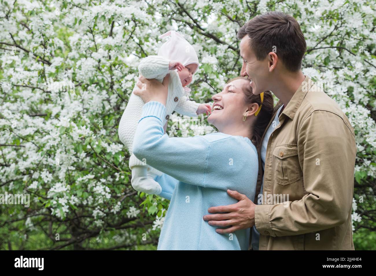 Mother raises smiling baby daughter and dad hugging his wife Stock