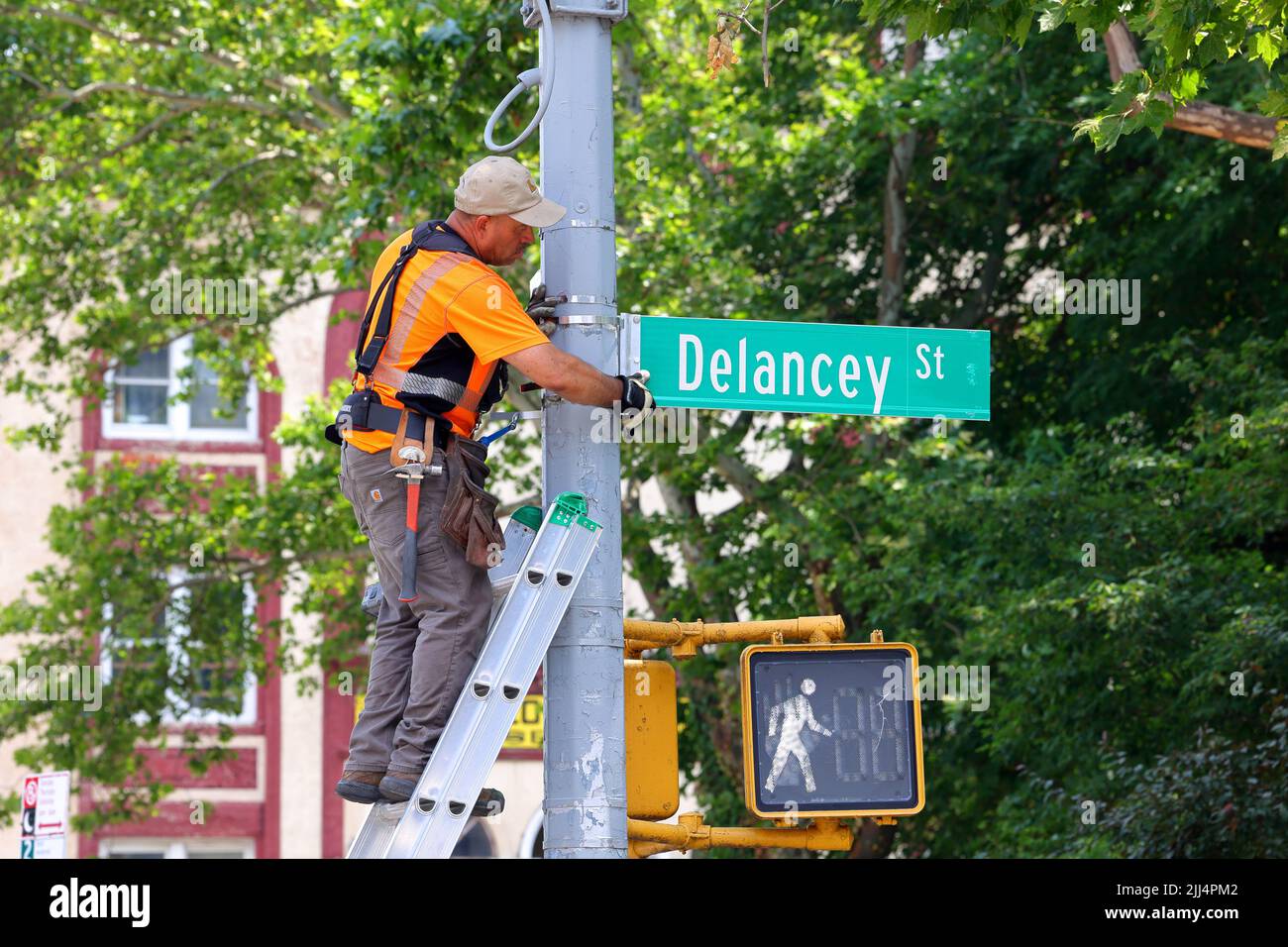 A worker on a ladder replacing a NYC street sign on a traffic pole in New York City. Stock Photo