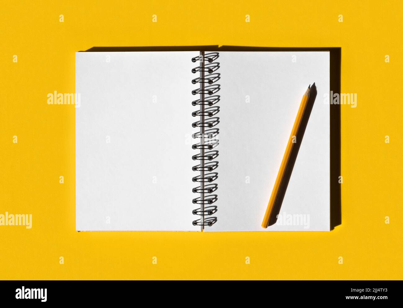 Notebook with pencil. School notebook on illuminated yellow background, spiral notepad on table. Top view of open notebook with blank pages Stock Photo