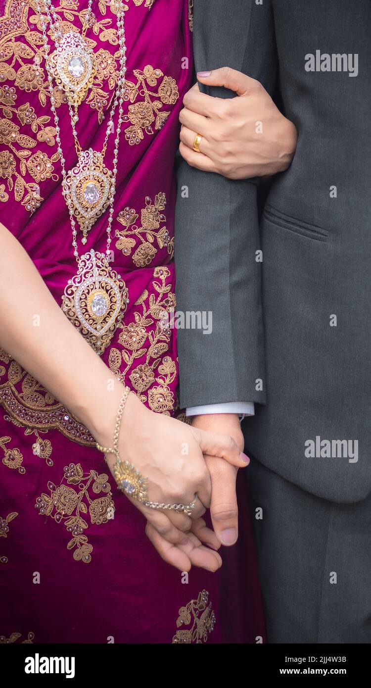 Bride holding groom's hand close up photo. Gold Jewelry and purple homecoming dress. Stock Photo
