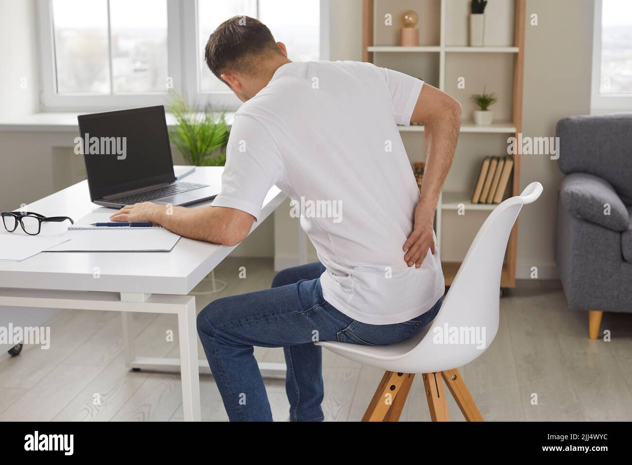 Man experiences severe back pain caused by prolonged and incorrect sitting at workplace. Stock Photo