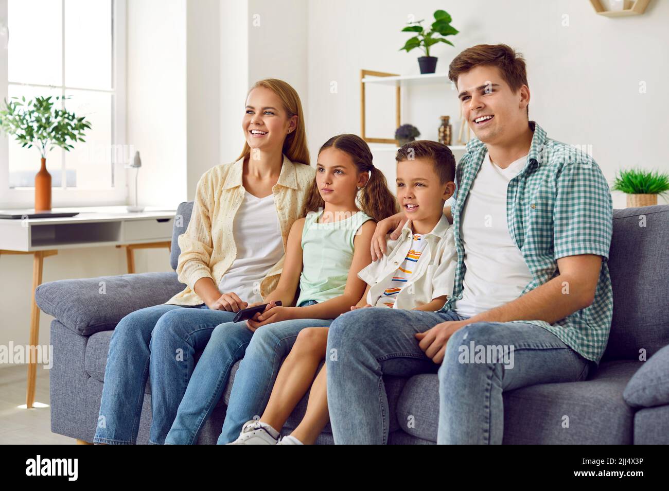 Happy mother, father and children sitting on the sofa at home and watching TV together Stock Photo