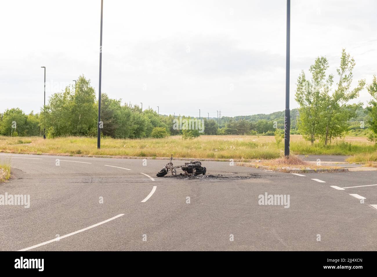 Newburn England: 16.06.2022: stolen motorbike set on fire burned out and abandoned on industrial estate Road with green trees Stock Photo