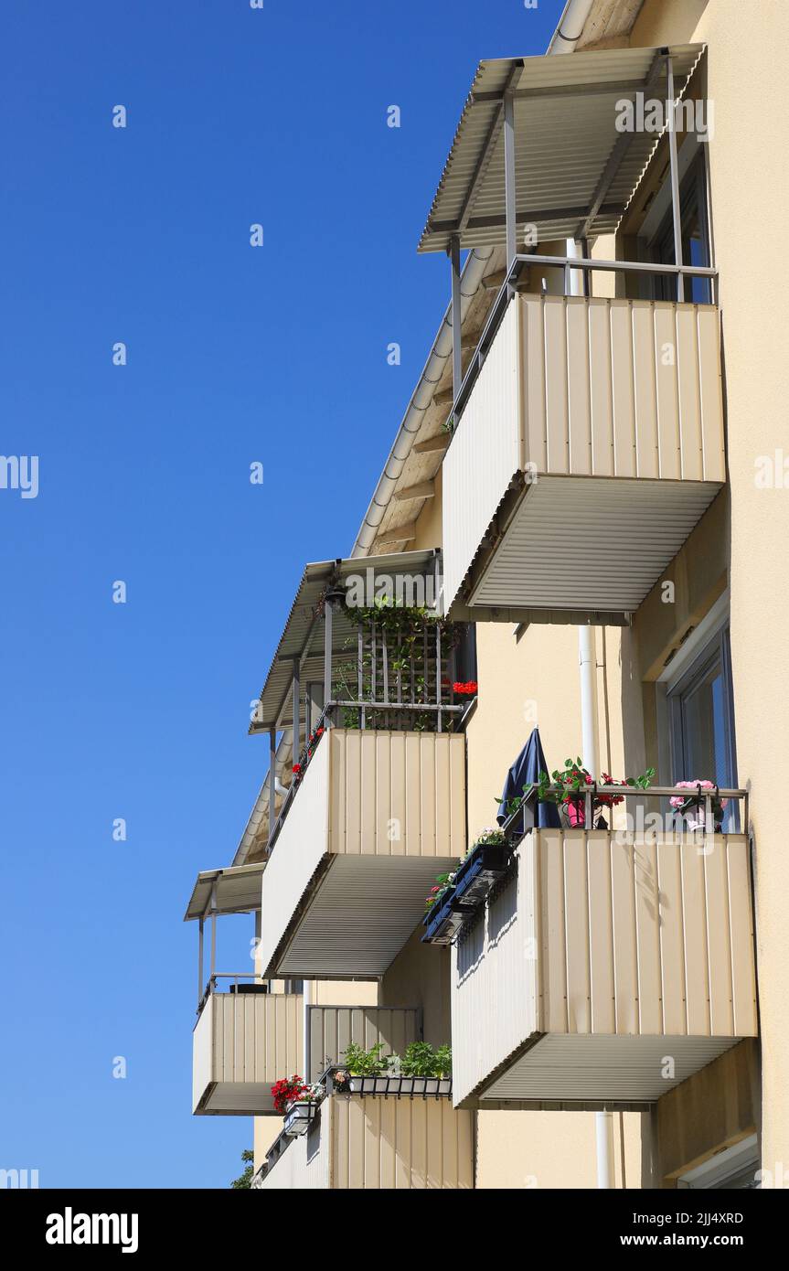 Side view of facade in multi-family building with apartments where some of the balconies have flower boxes with blooming flowers. Stock Photo