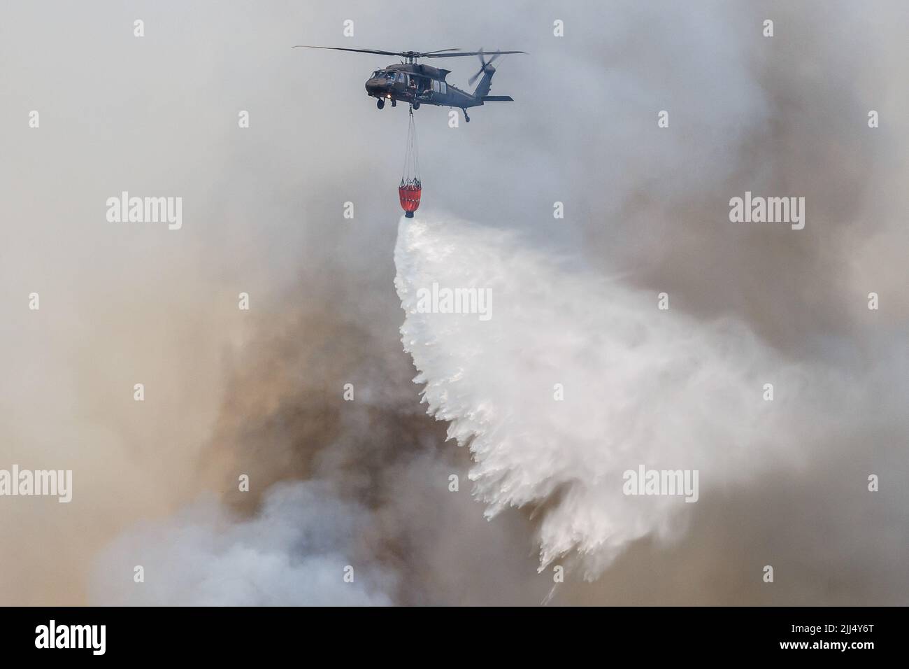 Karst, Slovenia. 22nd July, 2022. A Slovakian Sikorsky UH-60 Black Hawk helicopter carrying a Bambi bucket for extinguishing fires drops water on a large wildfire that burns near the village of Novelo in the Karst region of Slovenia. About a thousand firemen with air support from three Slovenian helicopters, two Serbian helicopters, an Austrian helicopter, a Slovakian Black Hawk helicopter and two Hungarian helicopters, a Croatian Canadair firefighting airplane and a Slovenian army Pilatus airplane continued battling a large wildfire that broke out five days ago and has intensified in the Kars Stock Photo