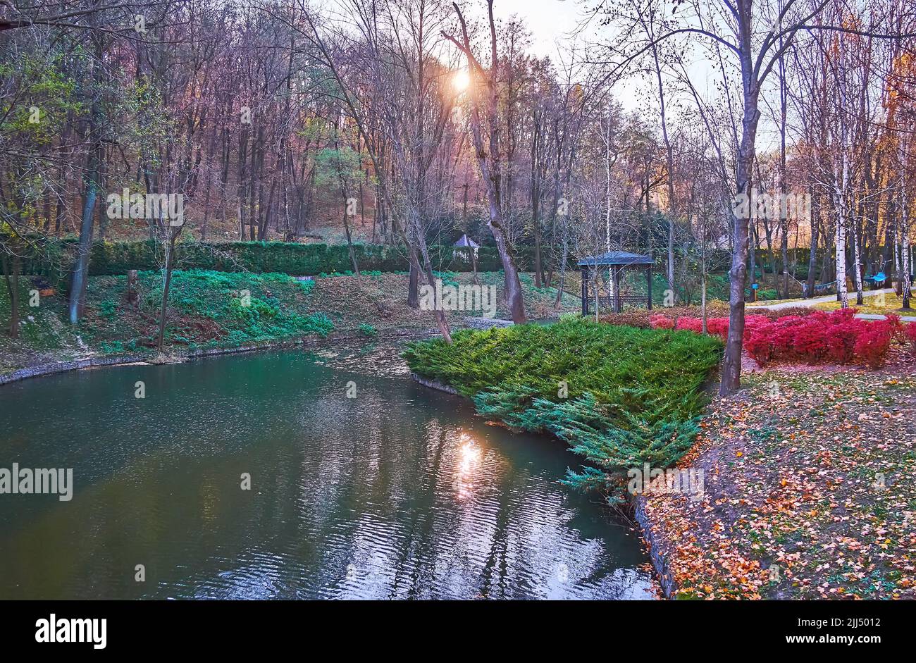 The dimmed sunset light in park with a curved river and tall autumn trees, Mezhyhirya, Ukraine Stock Photo