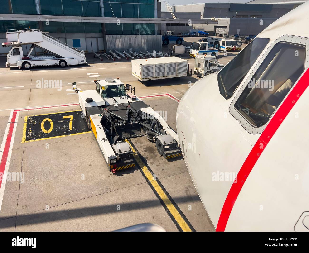 View from side of airplane cockpit on airfield with ground handling vehicles. No people. Aviation travel background with copy space. Airport gate 07 Stock Photo