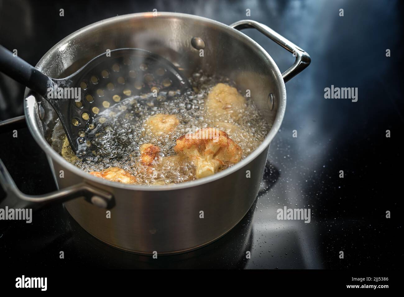 Deep frying cauliflower florets in a pot with boiling cooking oil on the stove, preparation of a tasty vegetable meal, copy space, selected focus, nar Stock Photo