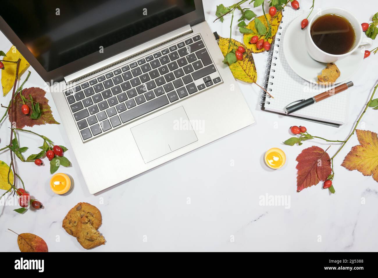 laptop computer, coffee cup, colorful autumn leaves and candles on a light gray marble table, seasonal home office desktop with copy space, high angle Stock Photo