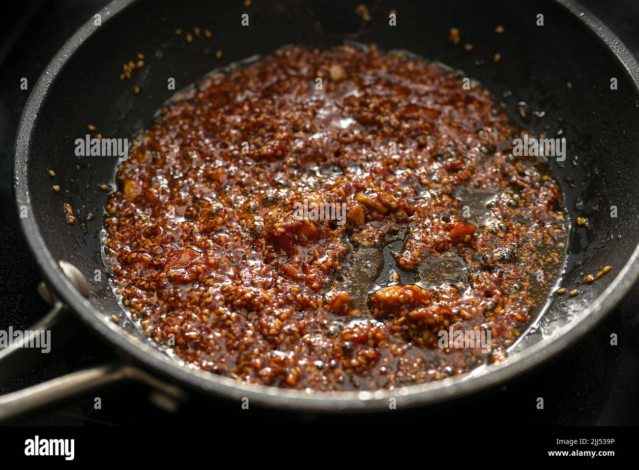Cooking a spicy sauce with ginger, garlic, chili, tomato paste and sesame seeds in vegetable oil in a pan, selected focus, very narrow depth of field Stock Photo