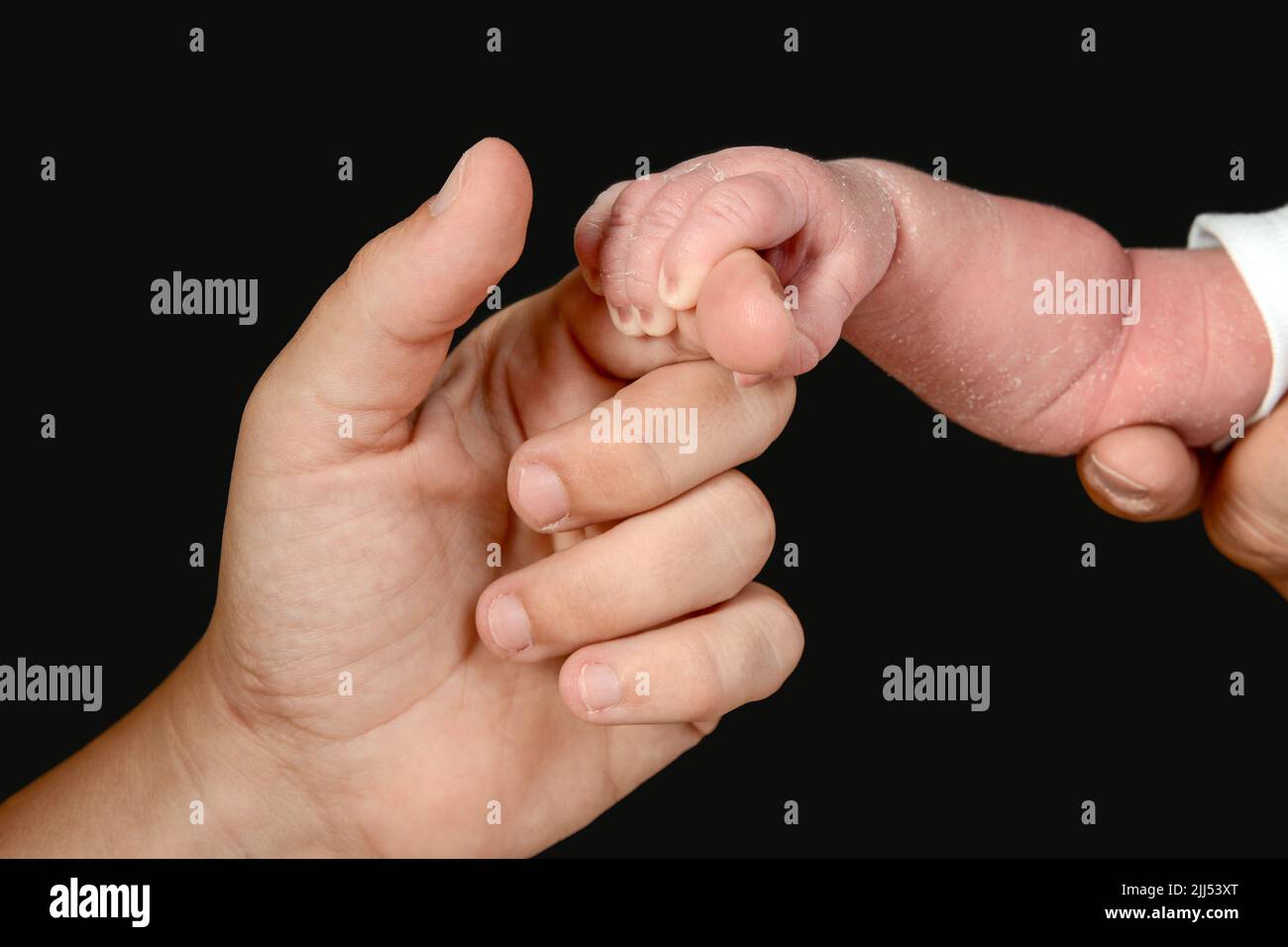 The small hand of a newborn caucasian baby grasps the hand of an adult person. Stock Photo