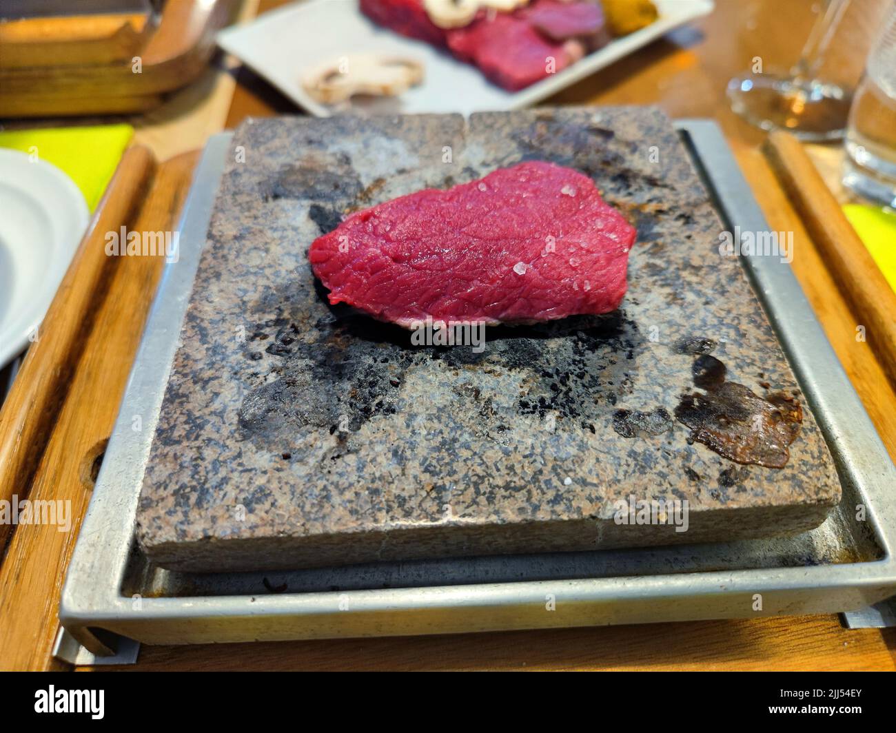 Raw steak is grilled on a stone grill with sauces in a restaurant on a dinner table Stock Photo