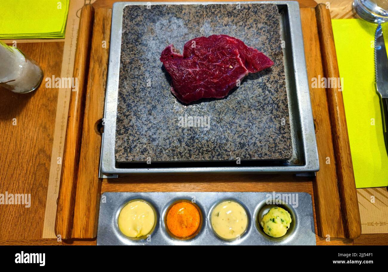 Raw steak is grilled on a stone grill with sauces in a restaurant on a dinner table Stock Photo
