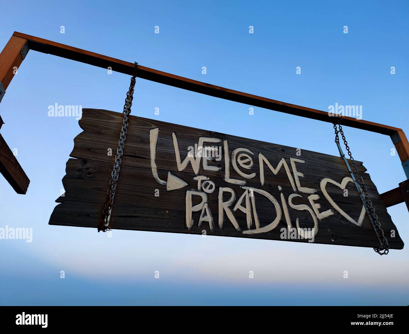Side shot of a wooden tropical Welcome to Paradise sign board with a beautiful blue sky background Stock Photo