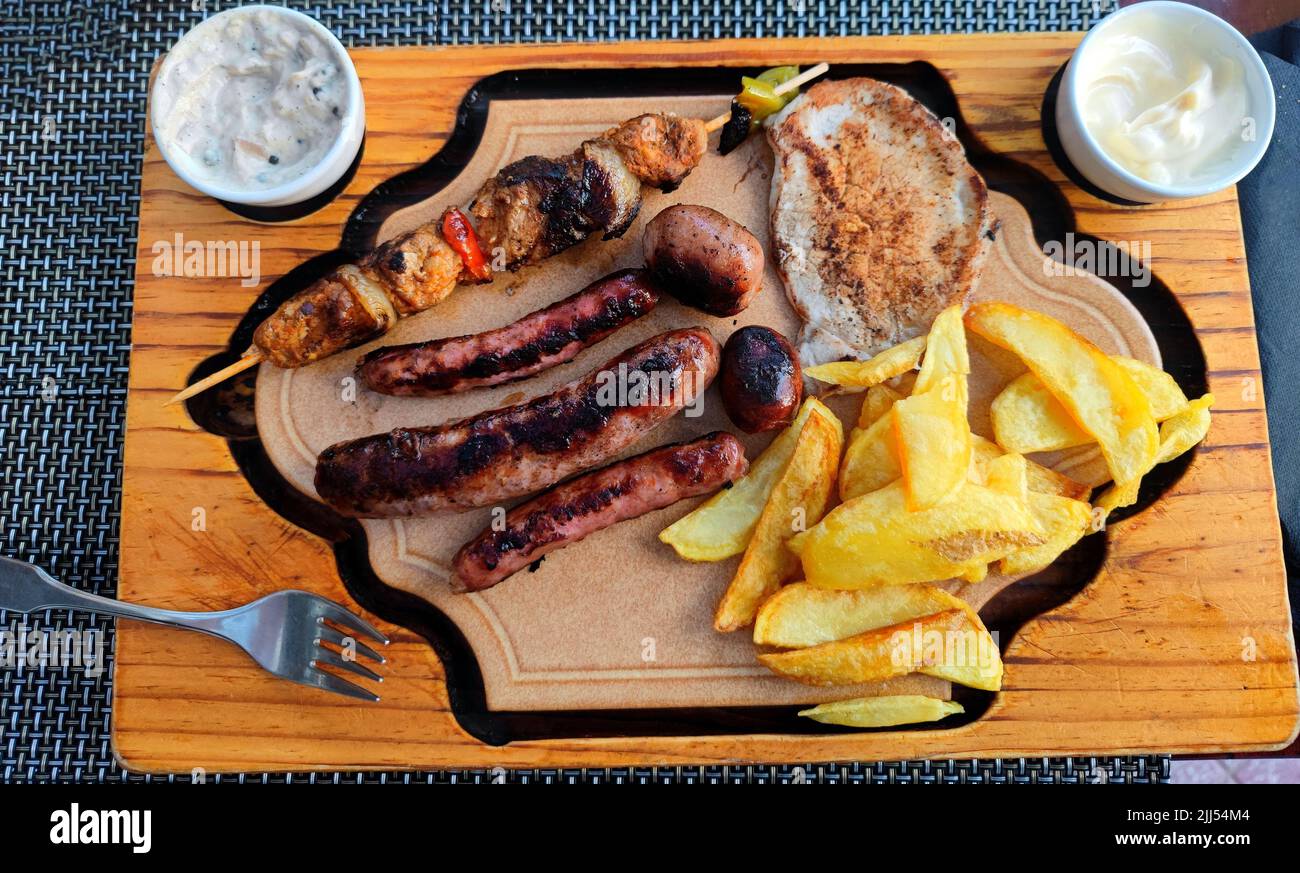 Delicious mixed grill consisting of different kinds of sausage, shish kebab, grilled chicken and fried potatoes served in a restaurant Stock Photo