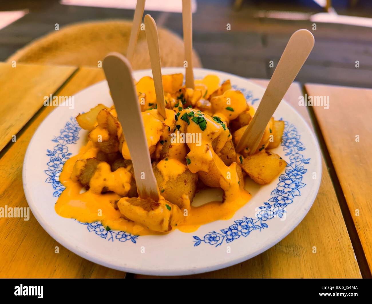 Delicious patatas bravas with spicy yellow traditional sauce served on a white board in a restaurant Stock Photo