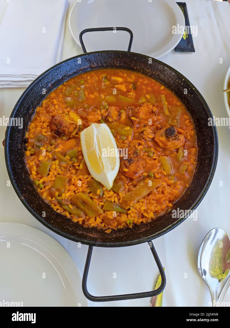 Delicious paella pan with vegetables, meat and a lemon on top served in a restaurant Stock Photo