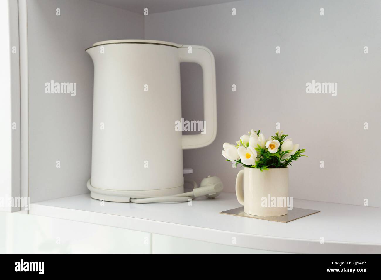 Cozy kitchen interior in Scandinavian style. White matte electric kettle and decorative flower on the shelf. Stock Photo