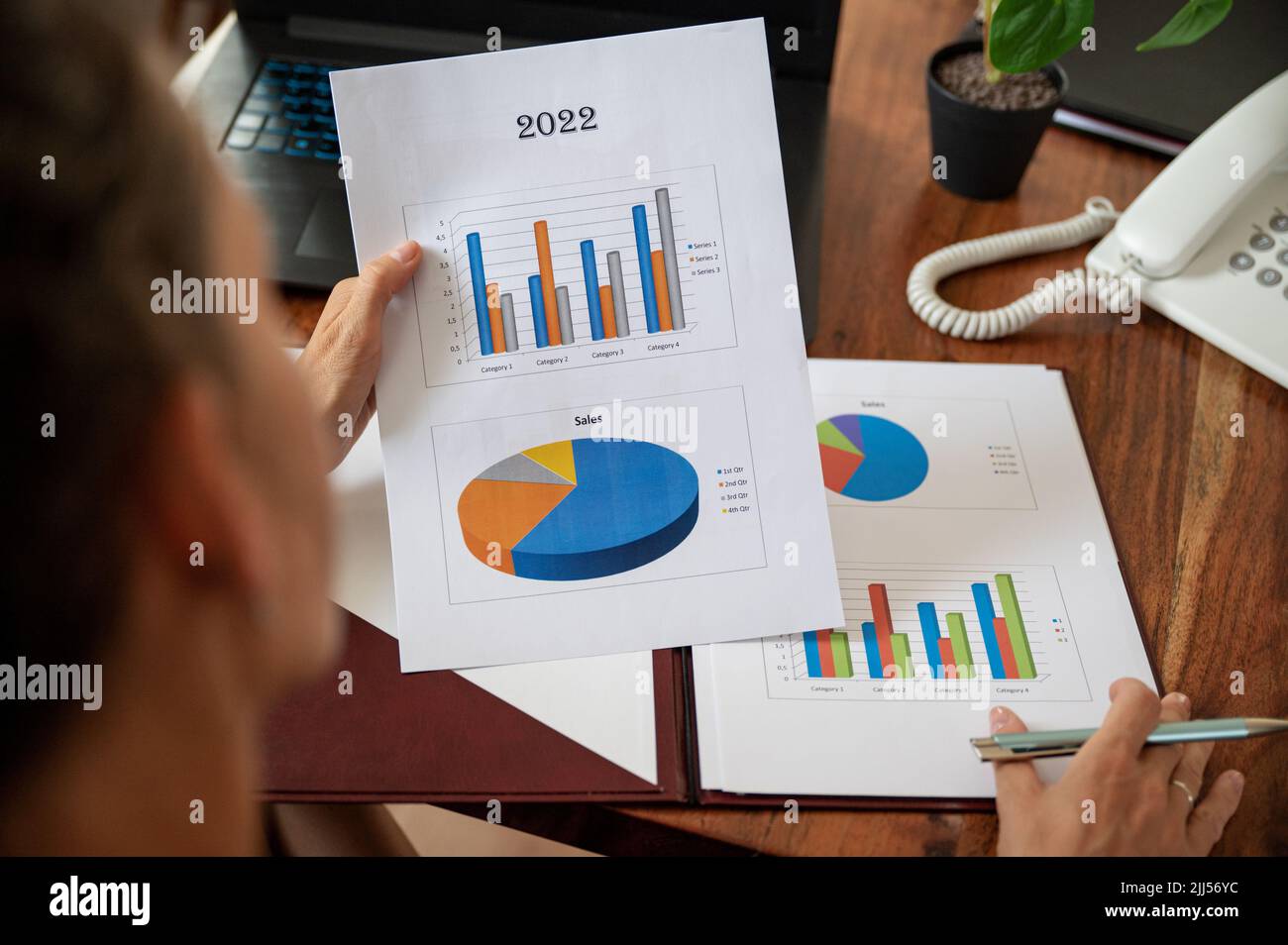 Overhead view of businesswoman reading and examining a statistical business report with colorful graphs and charts. Stock Photo