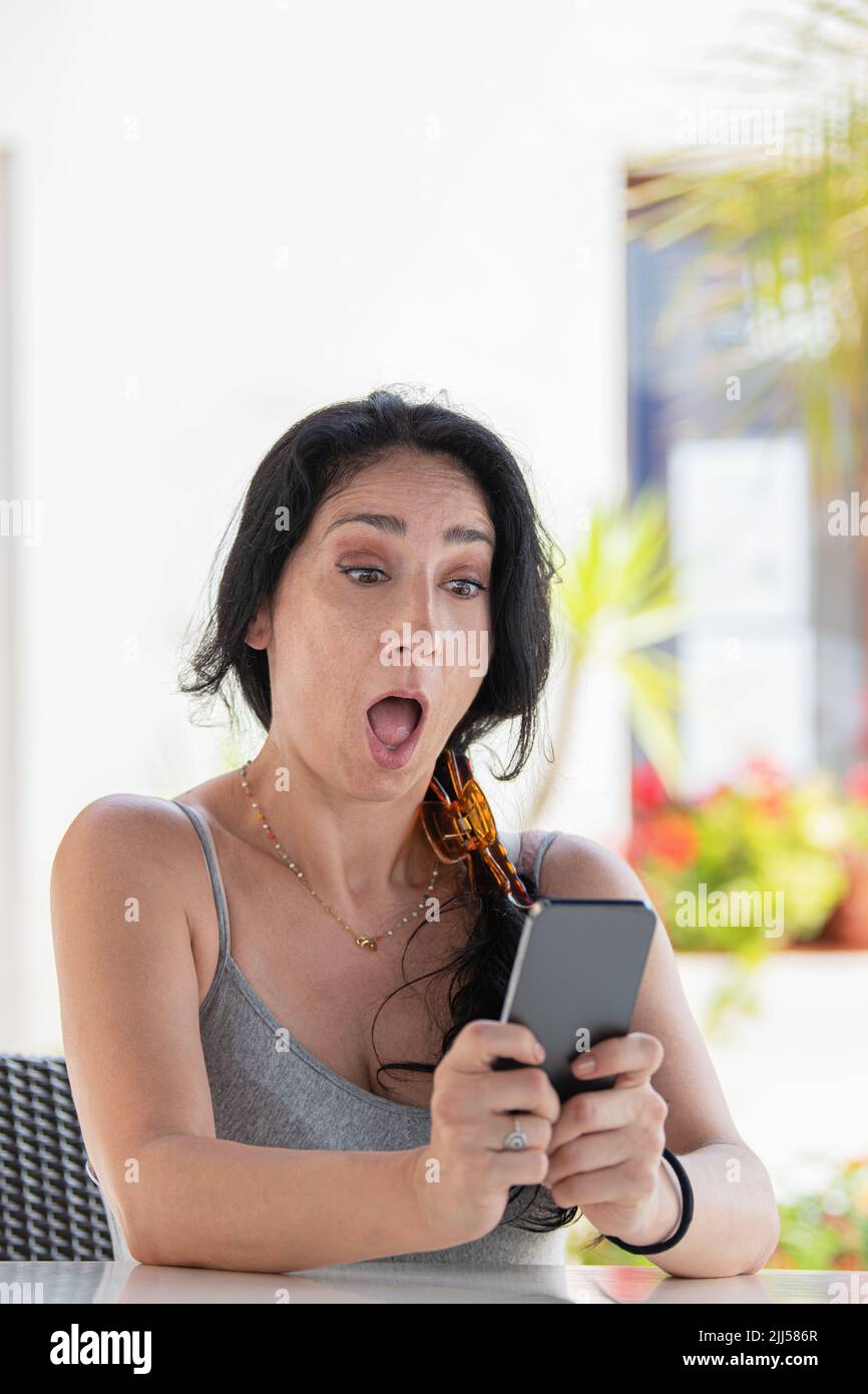 Amazed adult woman sitting looking her phone outside Stock Photo