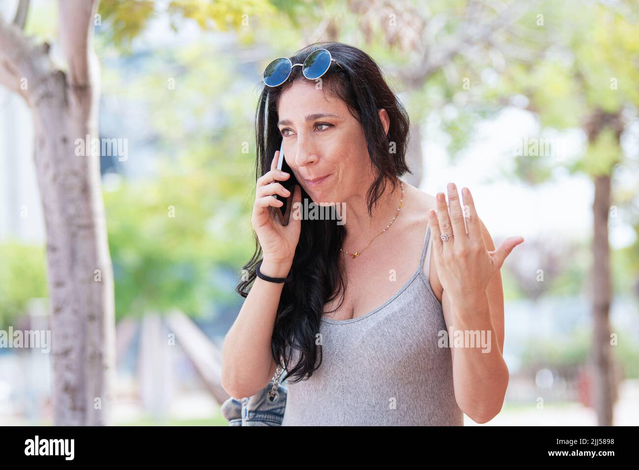 Adult woman on the street talking on the phone while gesturing with her other hand Stock Photo