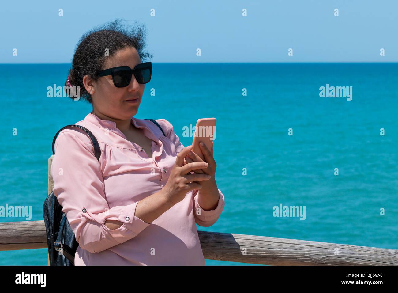 Focused woman with glasses checking her phone near the sea Stock Photo
