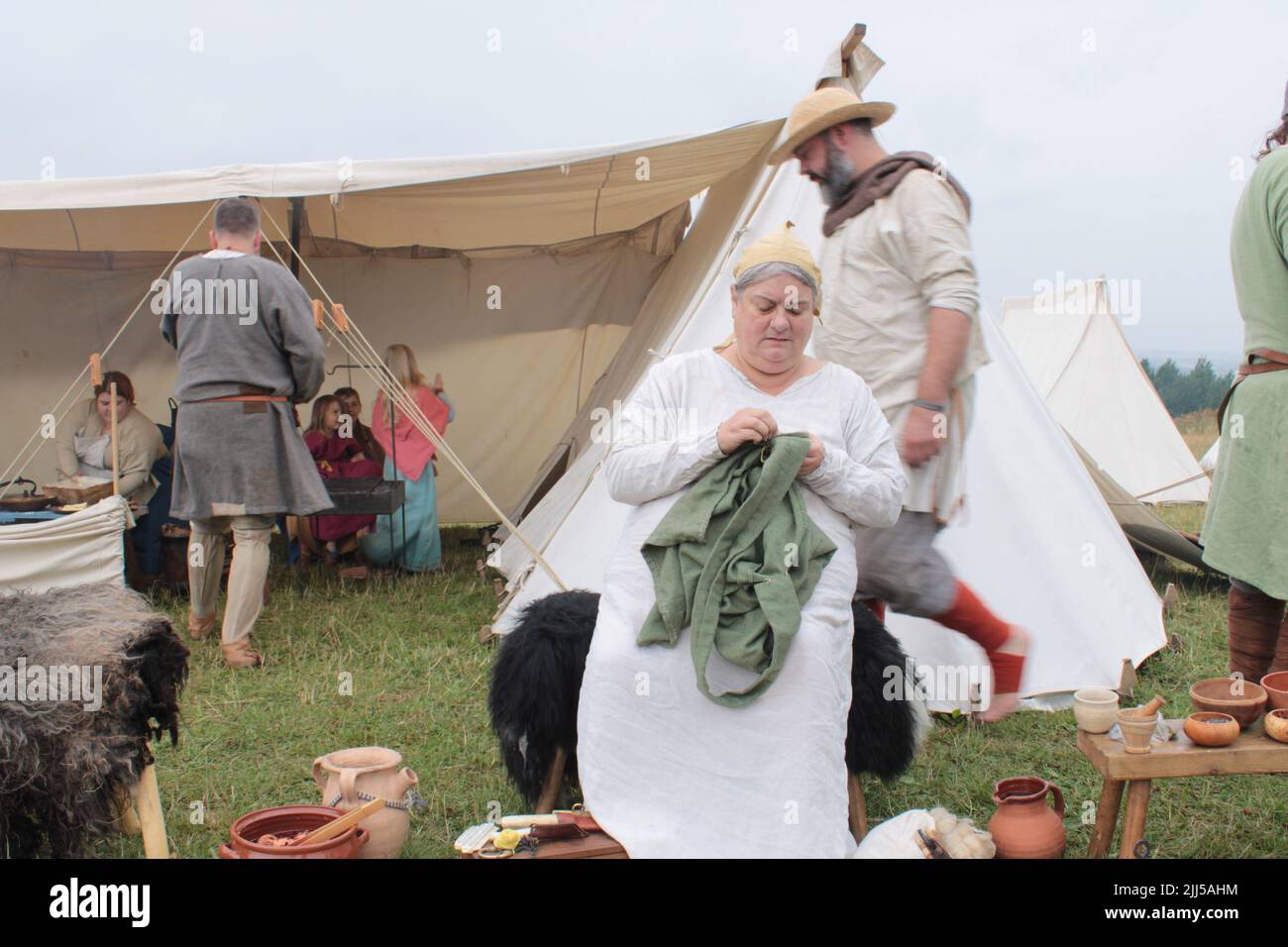 Viking peasant hand sewing a garment with encampment in the background.  Upholland green fayre, Lancashire, England 23-07-2022 Stock Photo