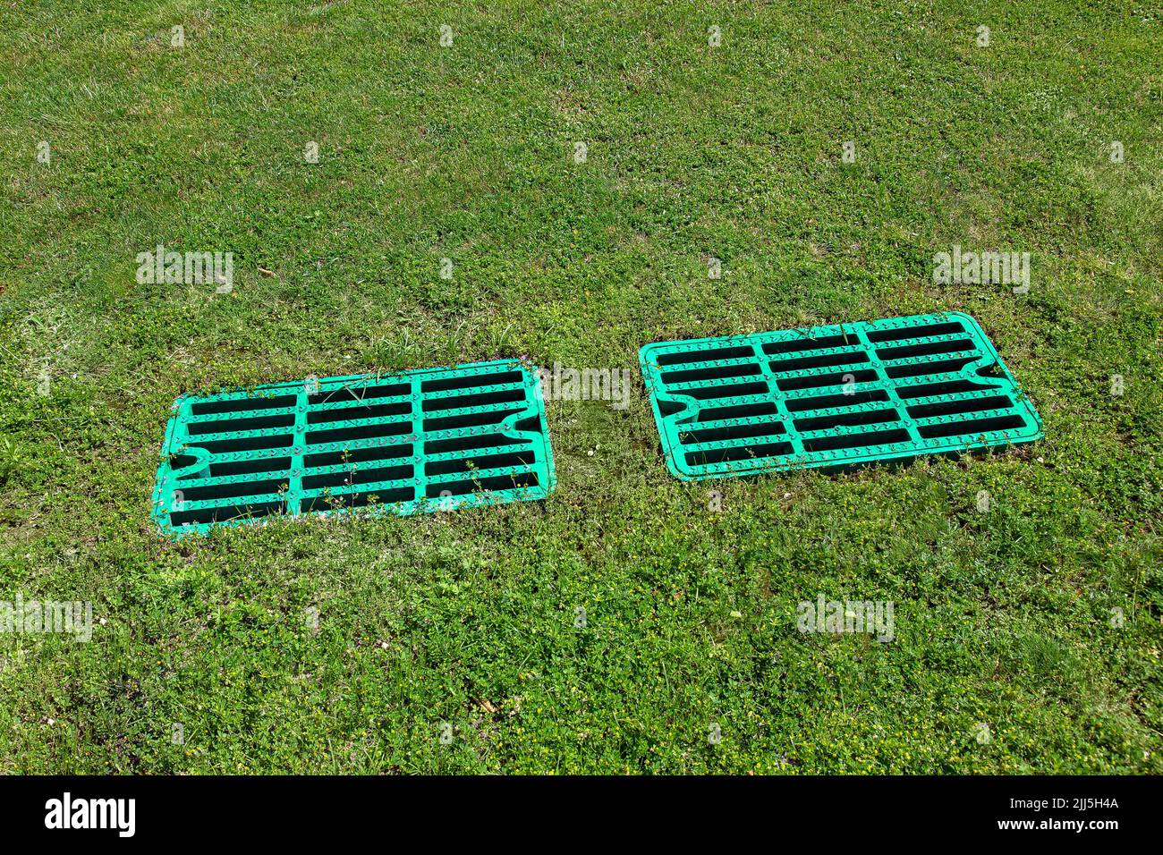2 manhole drainage grates on the lawn with green grass septic tank cover, sump cesspool drainage system environment design, close up view lit by sun o Stock Photo