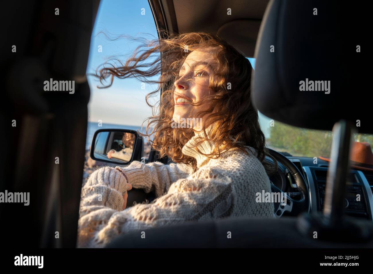 Smiling woman with tousled hair sitting in car Stock Photo