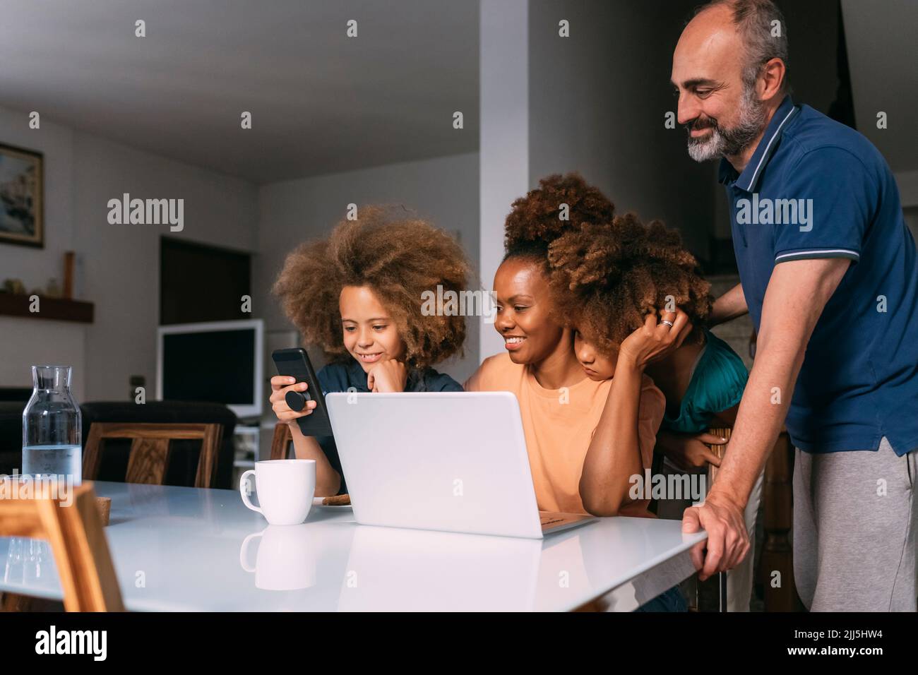 Smiling parents looking at boy using smart phone sitting at table Stock Photo