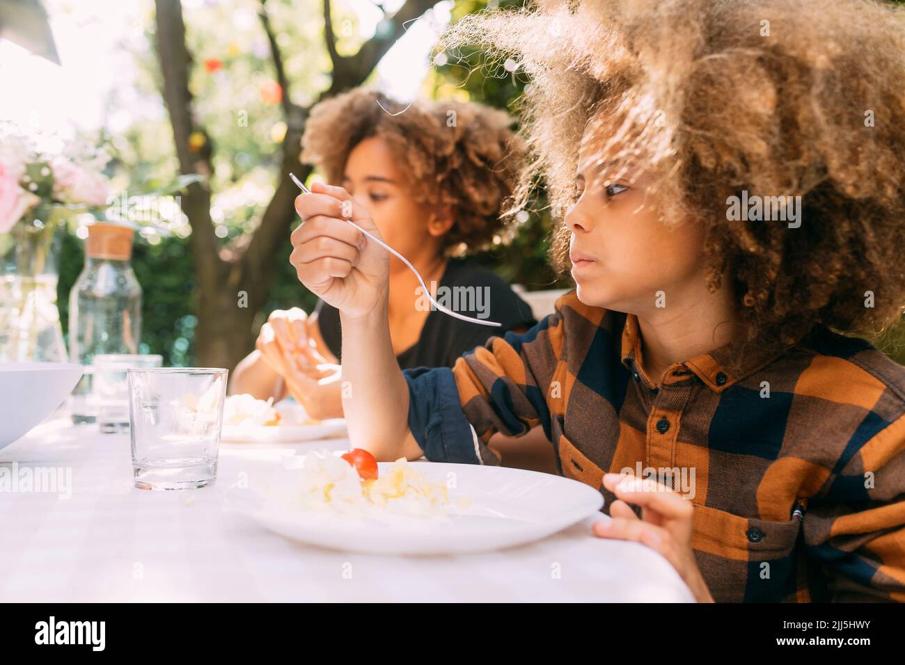 Boy with sister eating lunch at dining table in yard Stock Photo