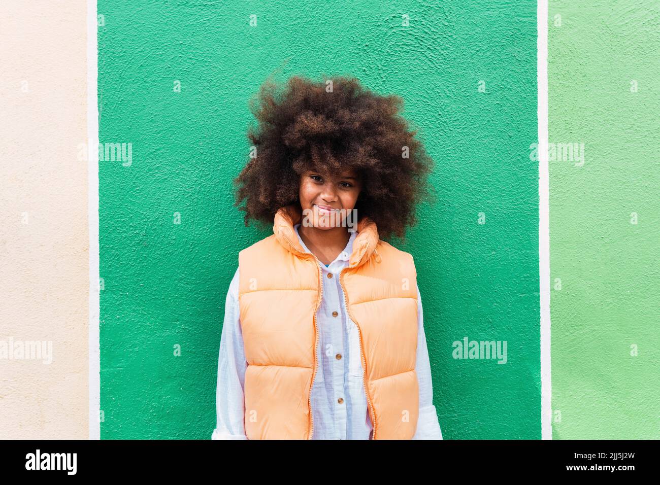 Smiling girl with Afro hairstyle standing in front of green wall Stock ...