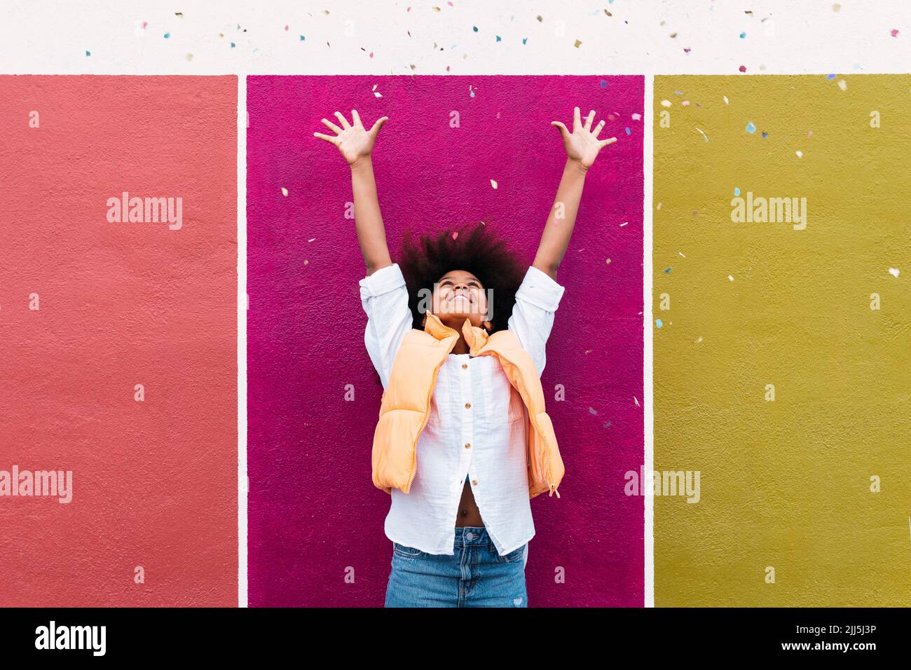 Girl with arms raised throwing confetti standing in front of colorful ...