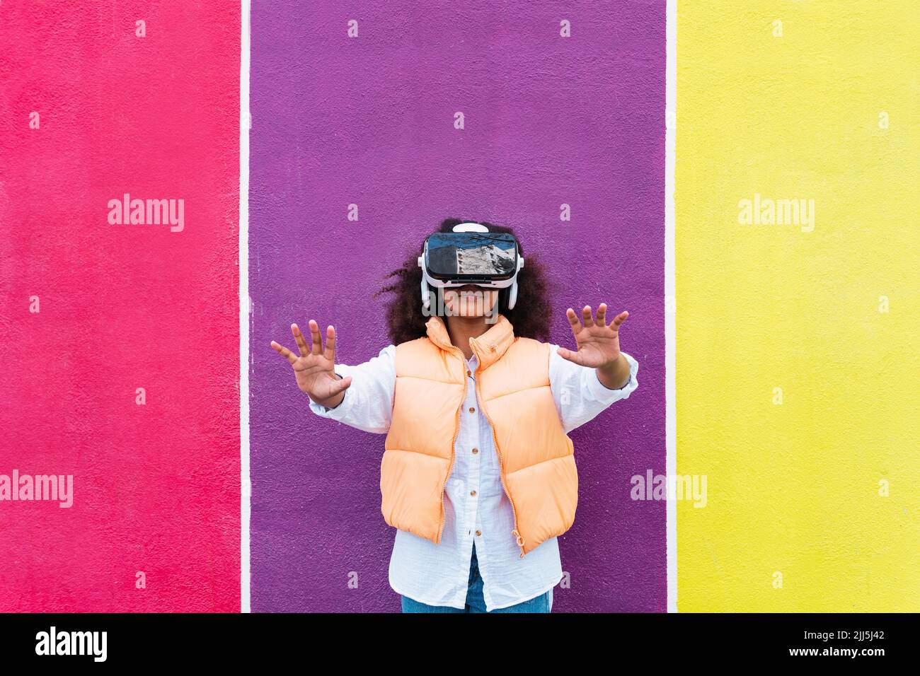 Girl wearing virtual reality simulator gesturing in front of colorful wall Stock Photo