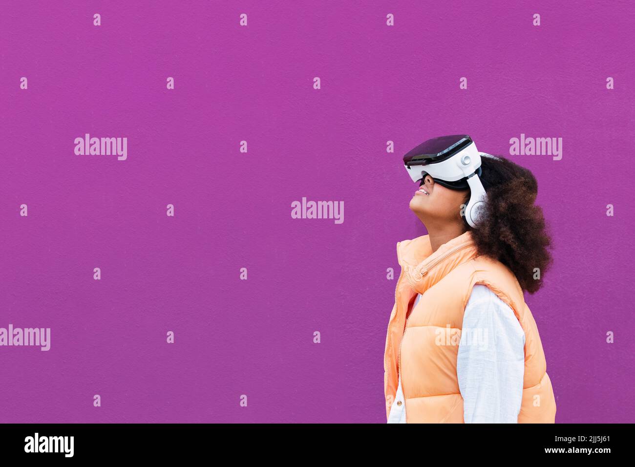 Girl wearing virtual reality simulator standing against purple