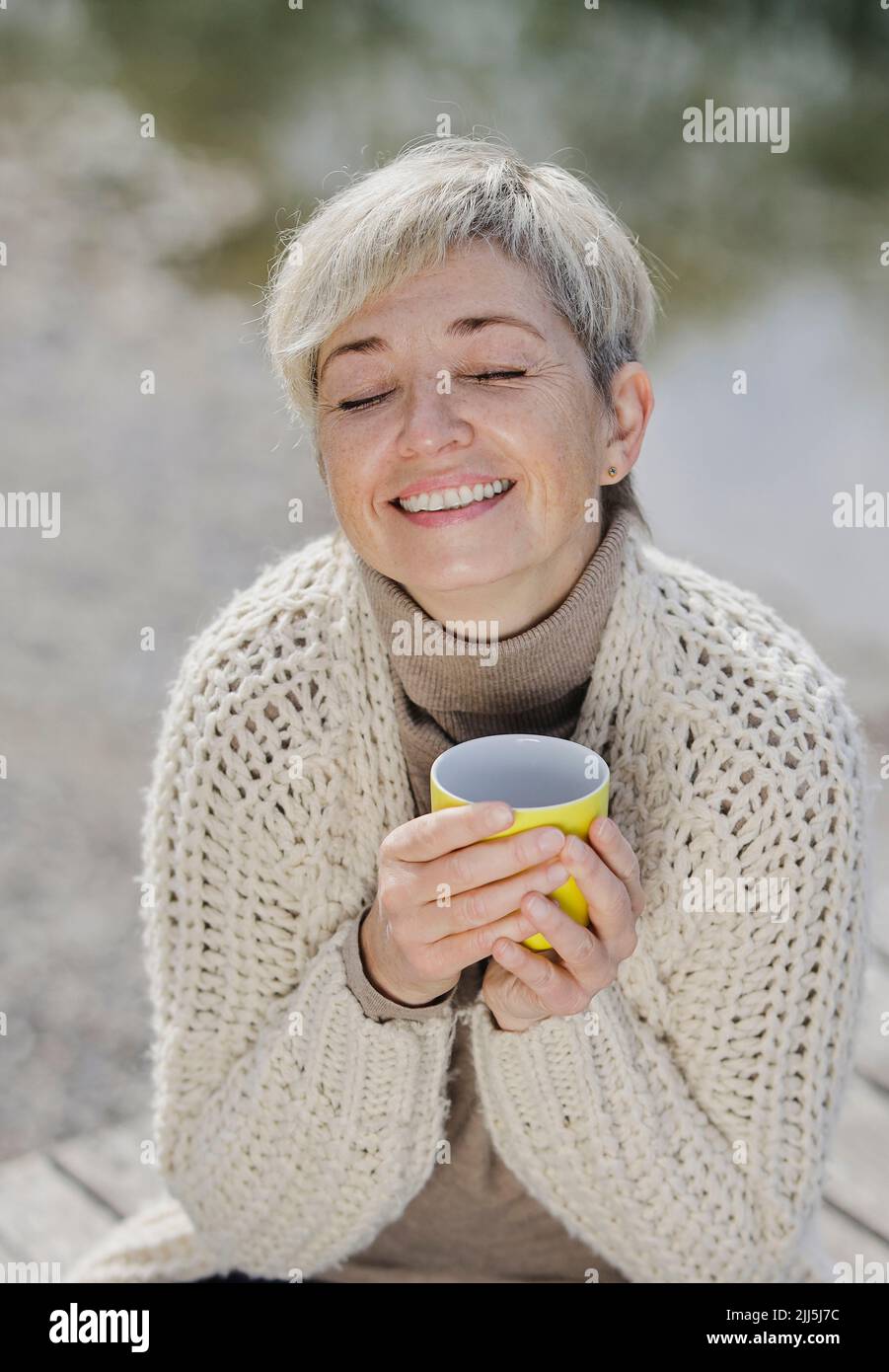 Smiling mature woman with eyes closed holding cup Stock Photo