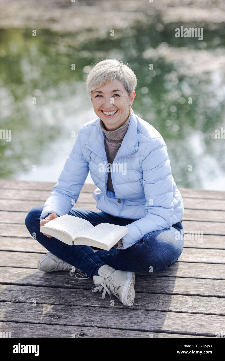 Happy woman with book sitting on pier Stock Photo
